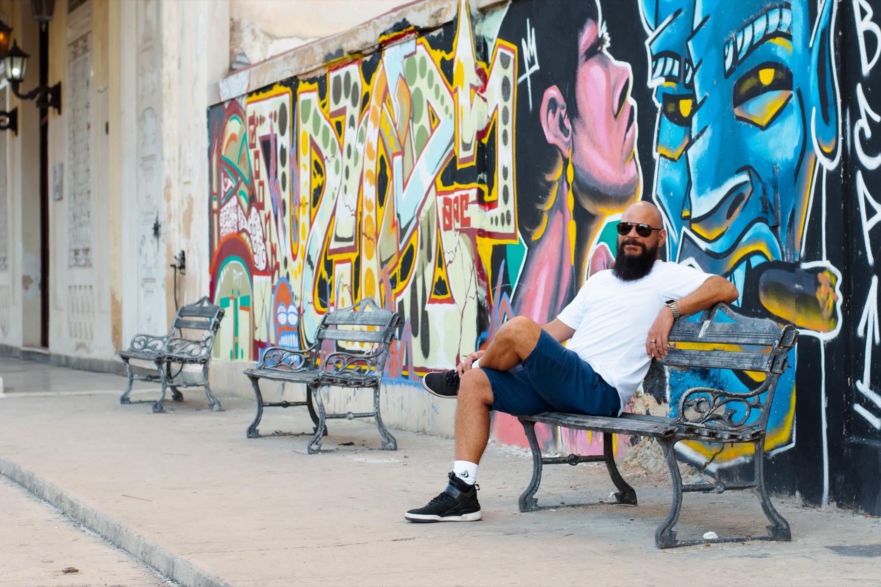 BOOSSOO sentado frente a un mural de colores en La Habana